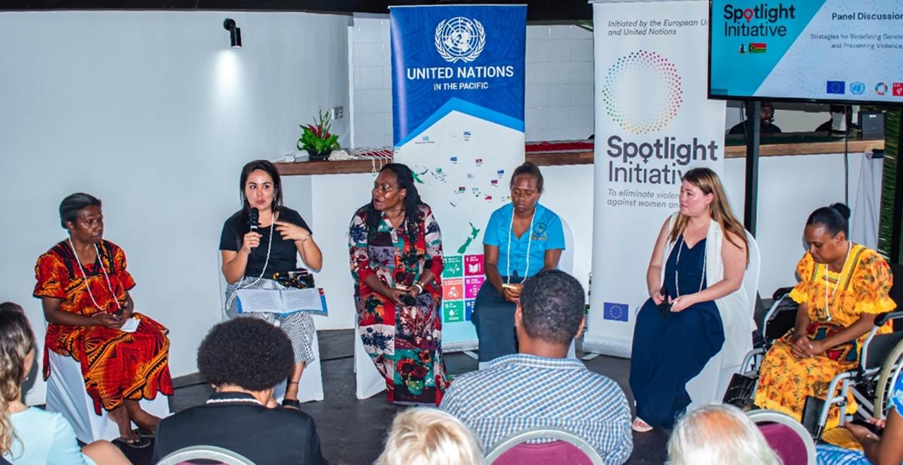 Six women panels sitting in front of audience, one of them, the moderator speaking with a microphone.