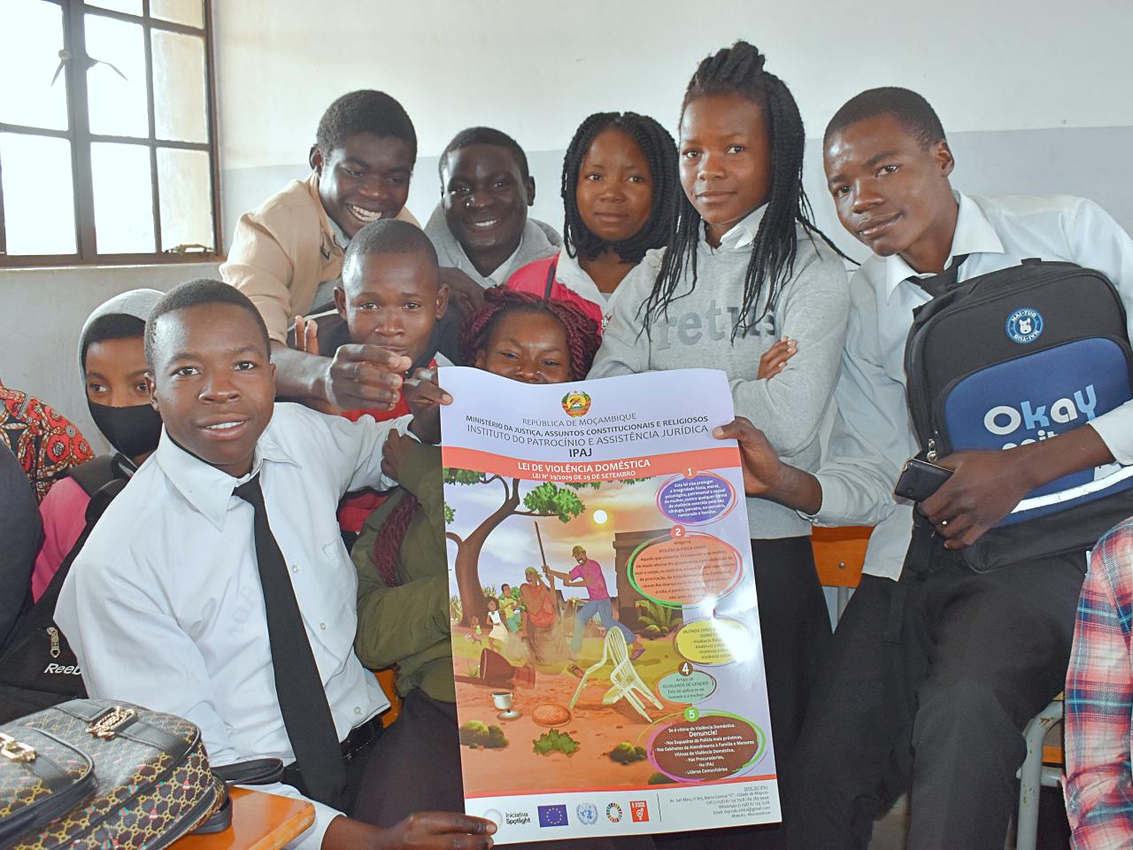 A group of students in a classroom hold a poster about the domestic violence law.