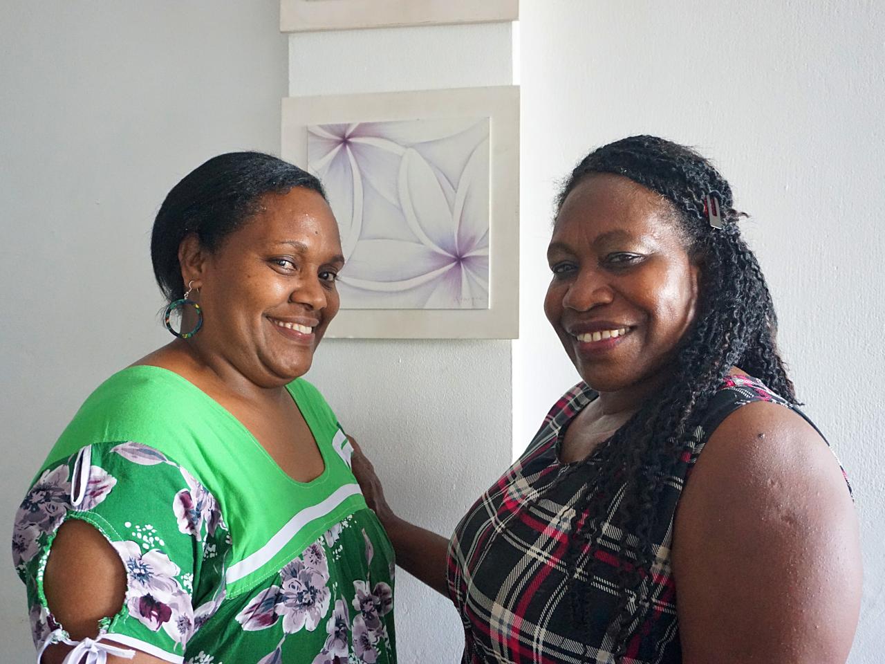 Two adult women facing each other, smiling and looking towards audience.