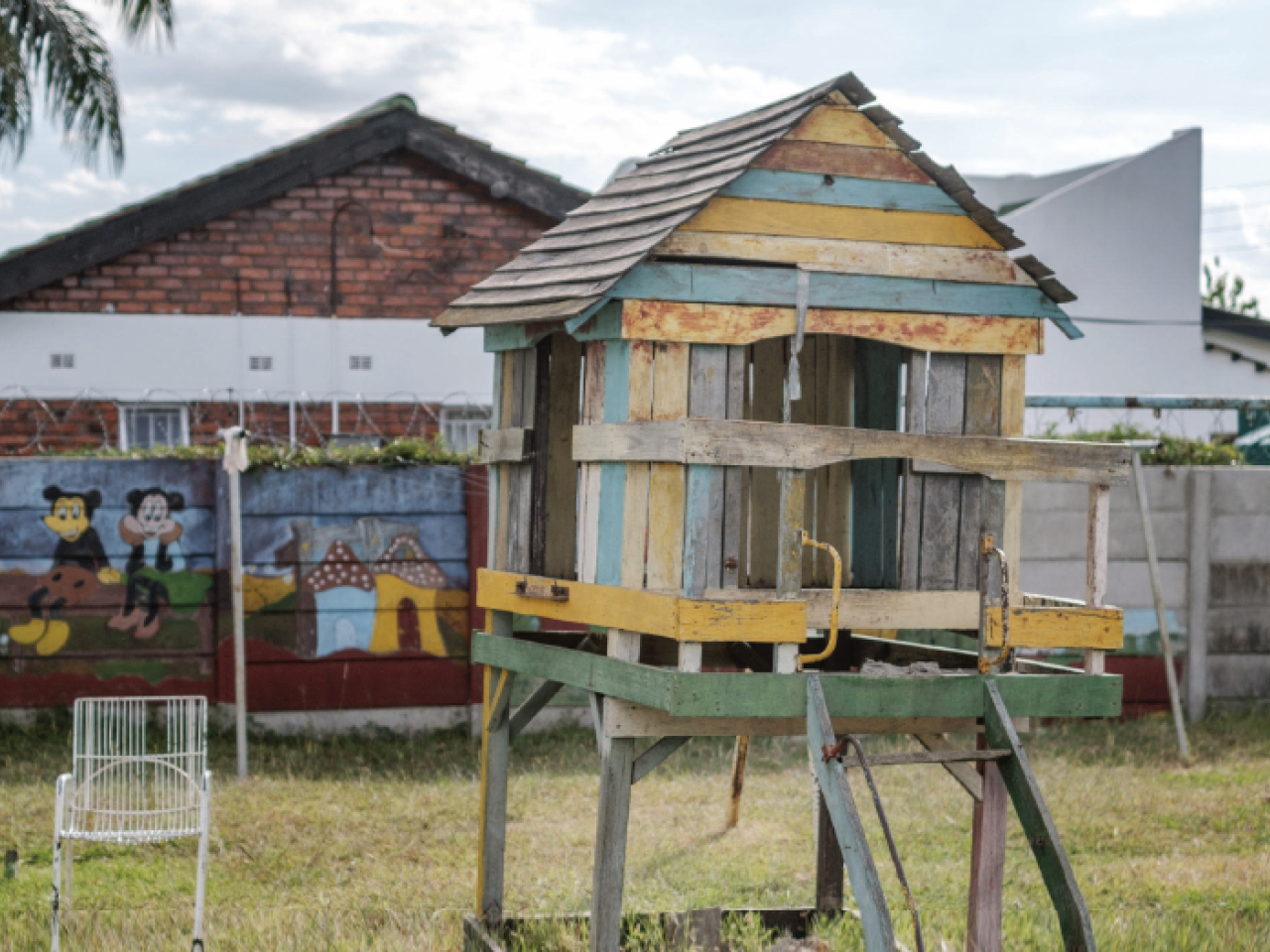 A children's playhouse stands in a grassy yard surrounded by a brightly painted fence