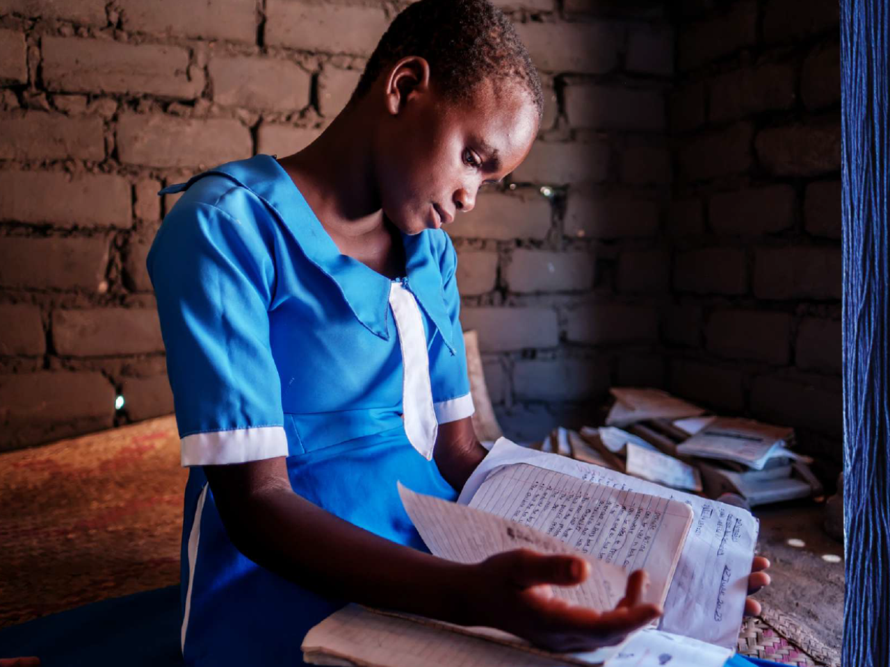Chikondi wears a school uniform and is seated reading a school book