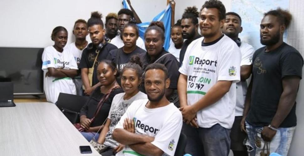 A group of young people smiling around a desk