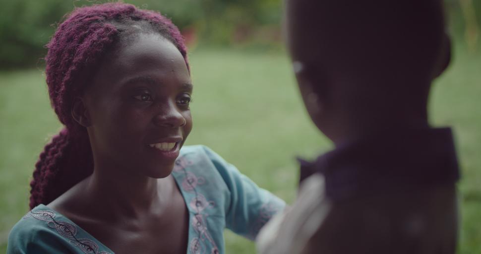 A smiling woman adjusts a young girl's school uniform