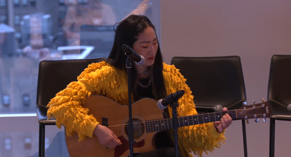 A woman in a yellow jacket playing guitar