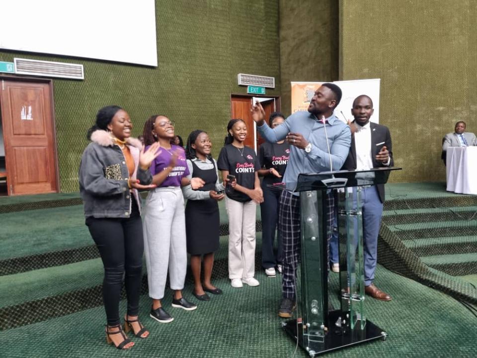 Person at lectern conducts choir of singers