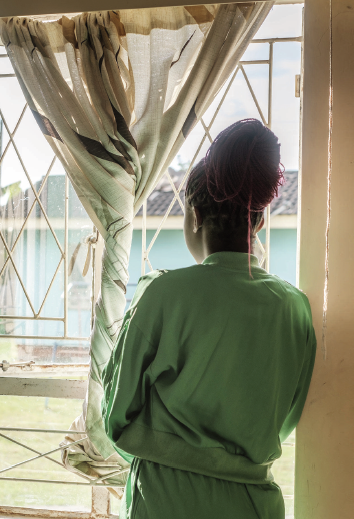 Rufaro wears a green tracksuit and looks out a window