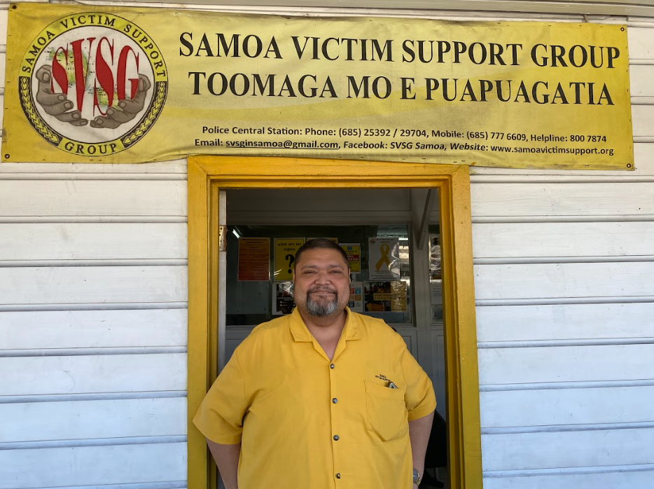 A man stands in a doorway wearing a yellow shirt