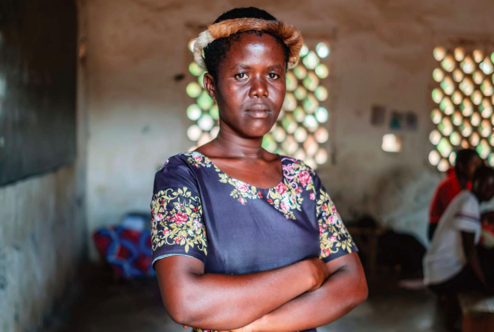 A young woman in a floral dress stands with her arms crossed