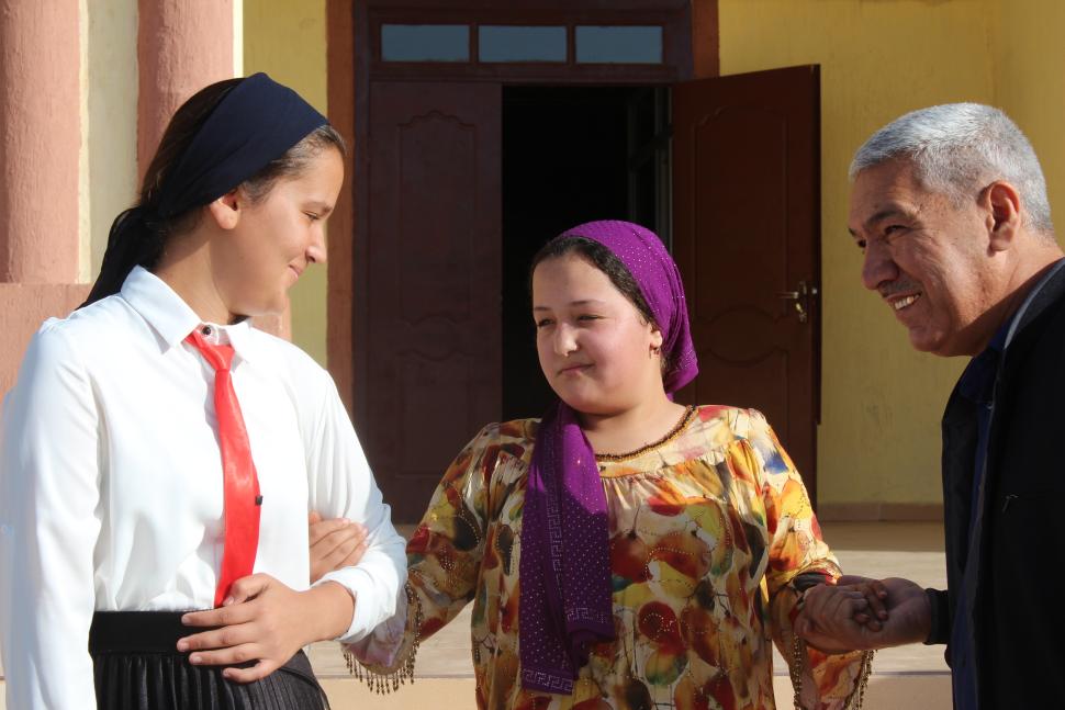 two girls linking arms stand beside an older man. 