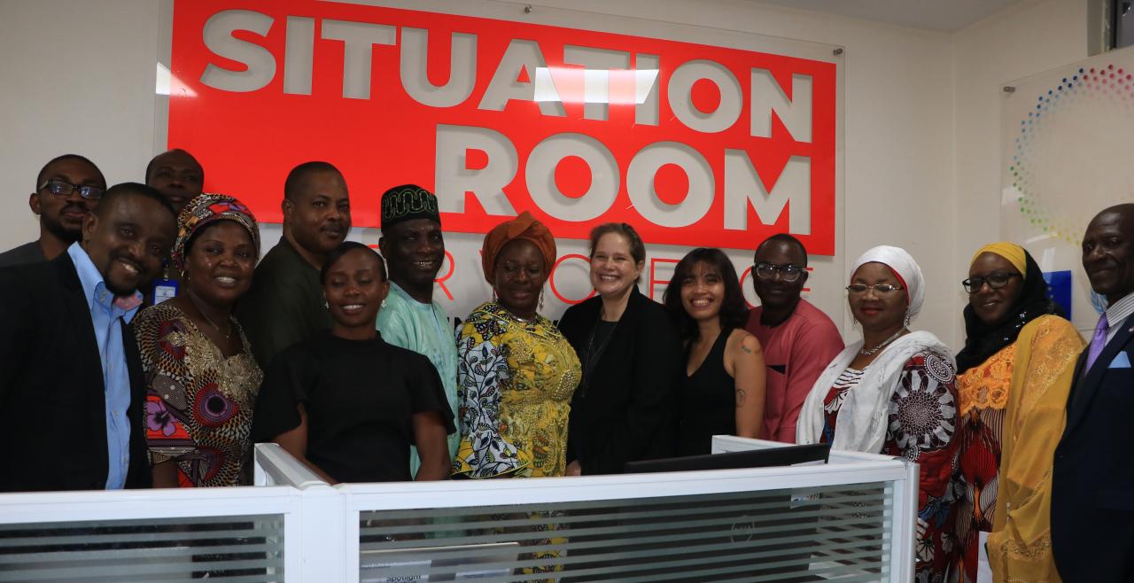 Men and women pose in front of situation room sign