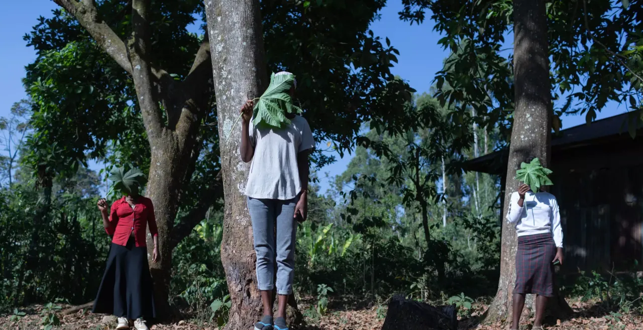 Three young women standing under a tree with faces obscured by leaves