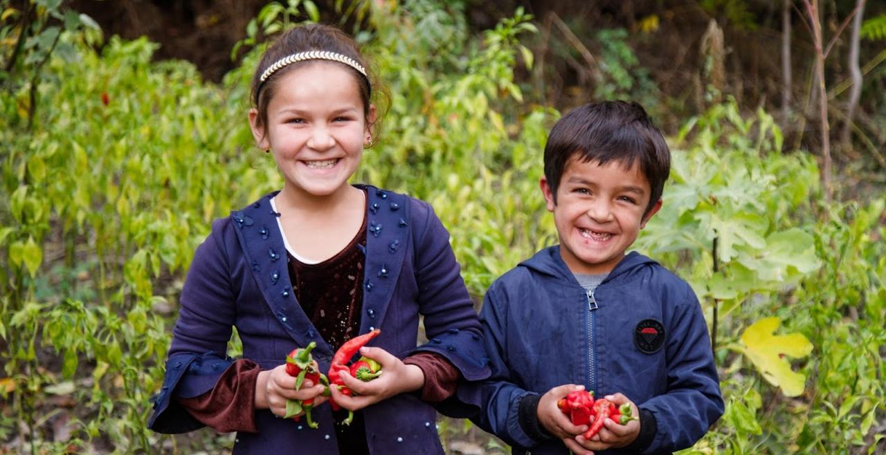 A girl and a boy smile in a garden holding vegetables