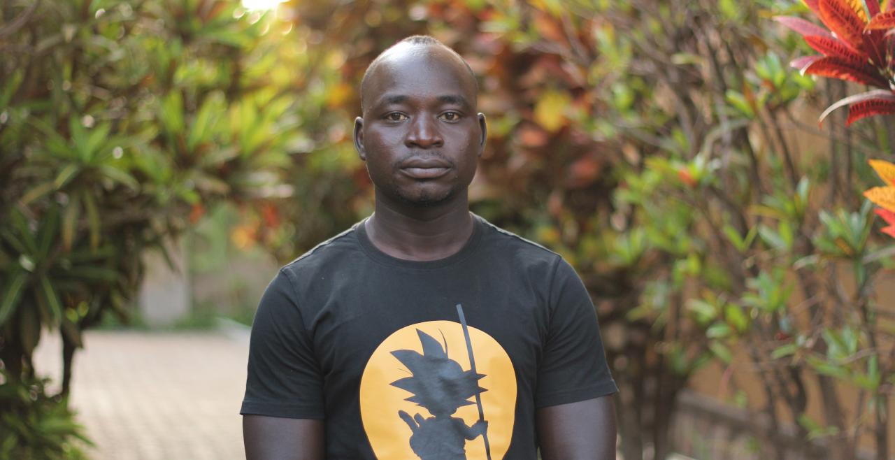 A man wearing a black t-shirt stands outside and looks into camera