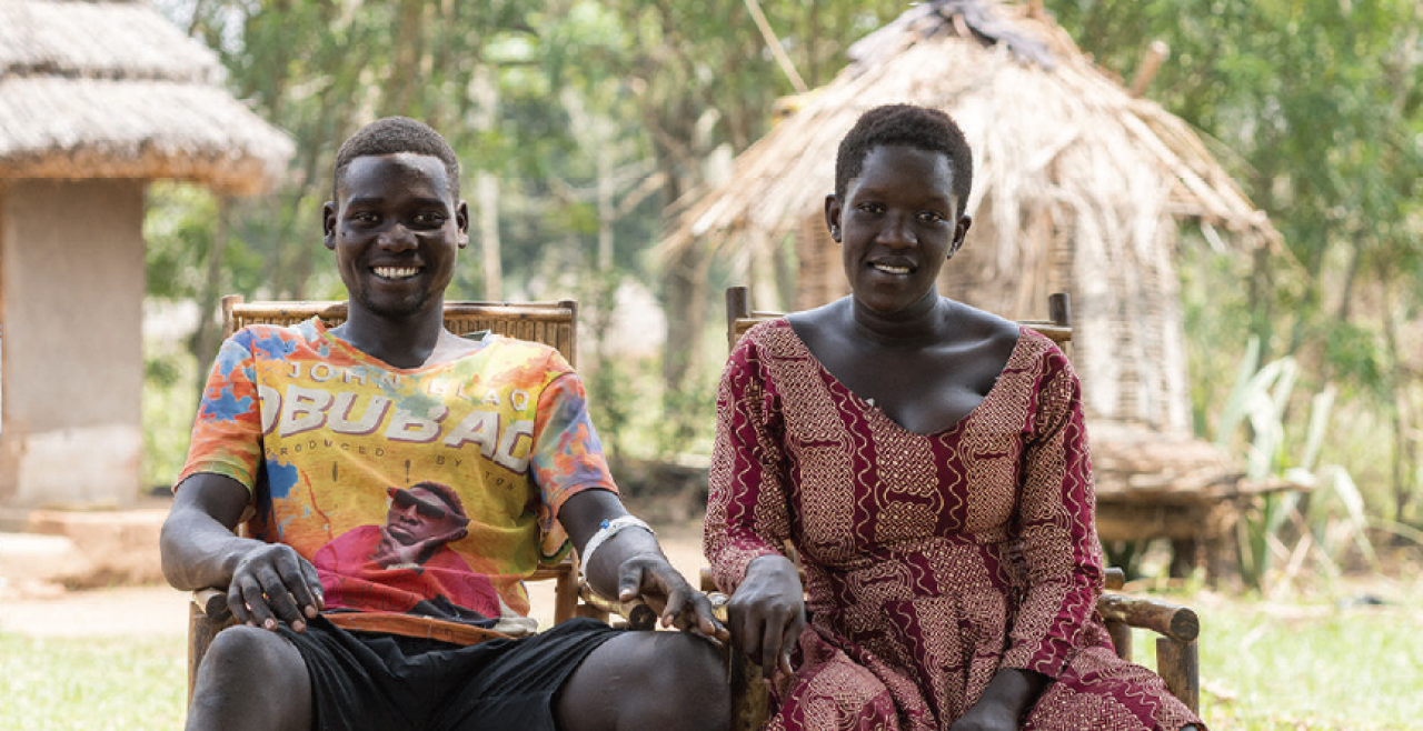 A man and a woman are seated, smiling and holding hands