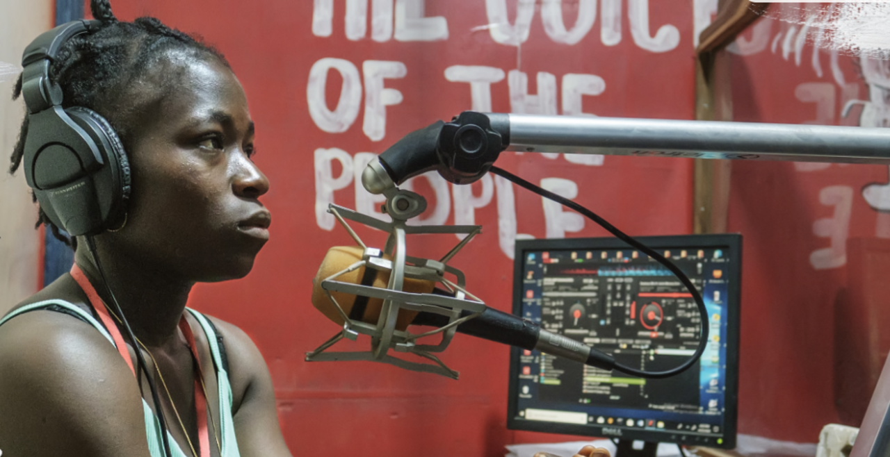 A woman in a radio studio sits in front of a mic
