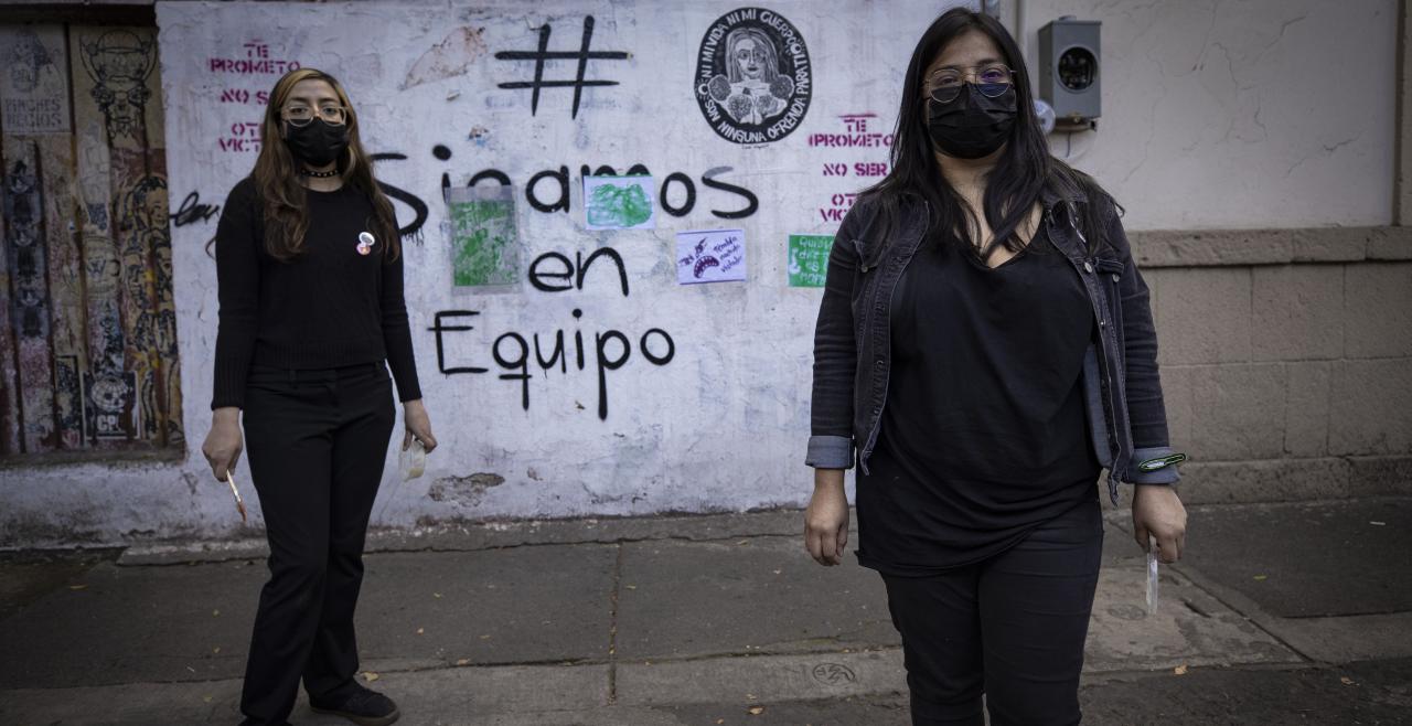 Two women stand in front of graffiti