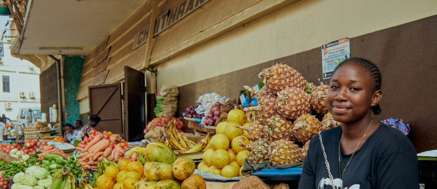 A smiling woman seated at a fruit stand