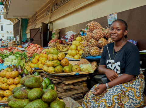 A smiling woman seated at a fruit stand